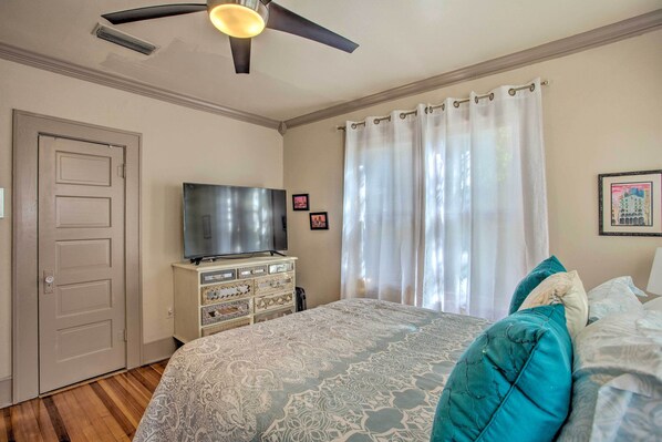 A bedroom with a bed, a television on a dresser, a ceiling fan, and a door.