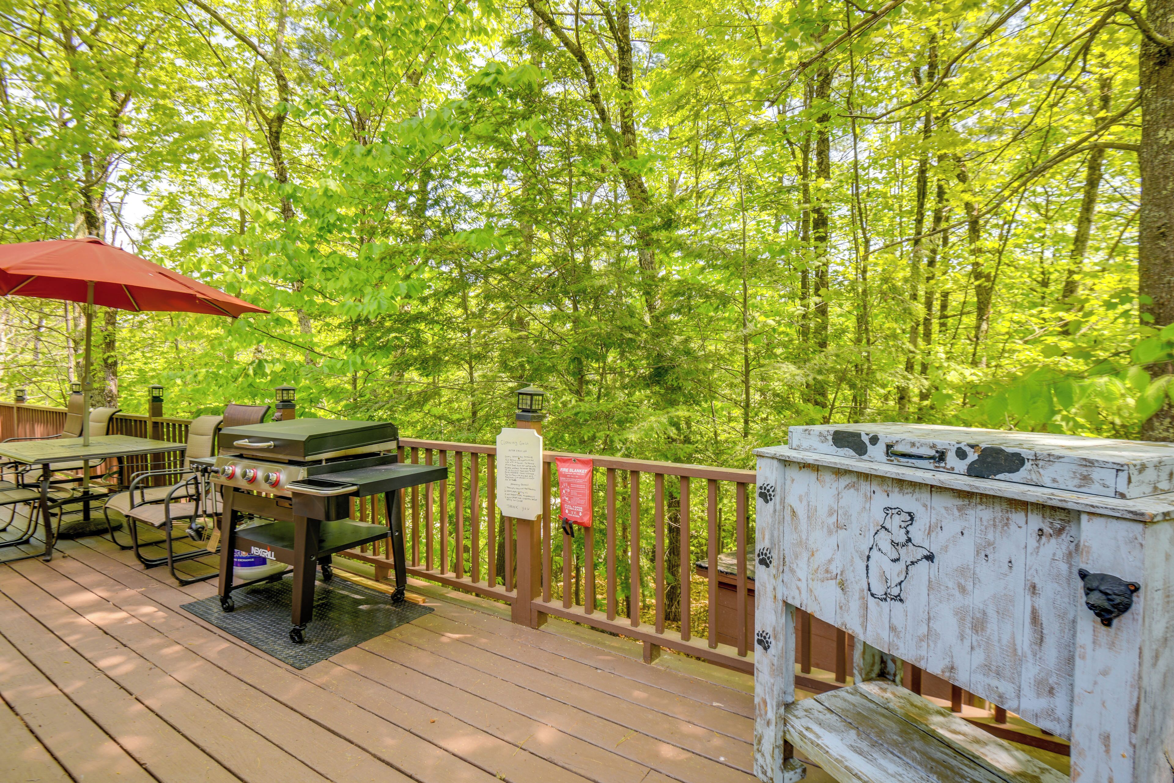A wooden deck with a grill, seating area, and a red umbrella.