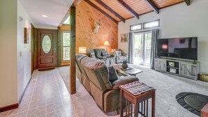 A cozy living room with a sofa, coffee table, and TV, wooden beams on the ceiling, and a door with a glass panel.