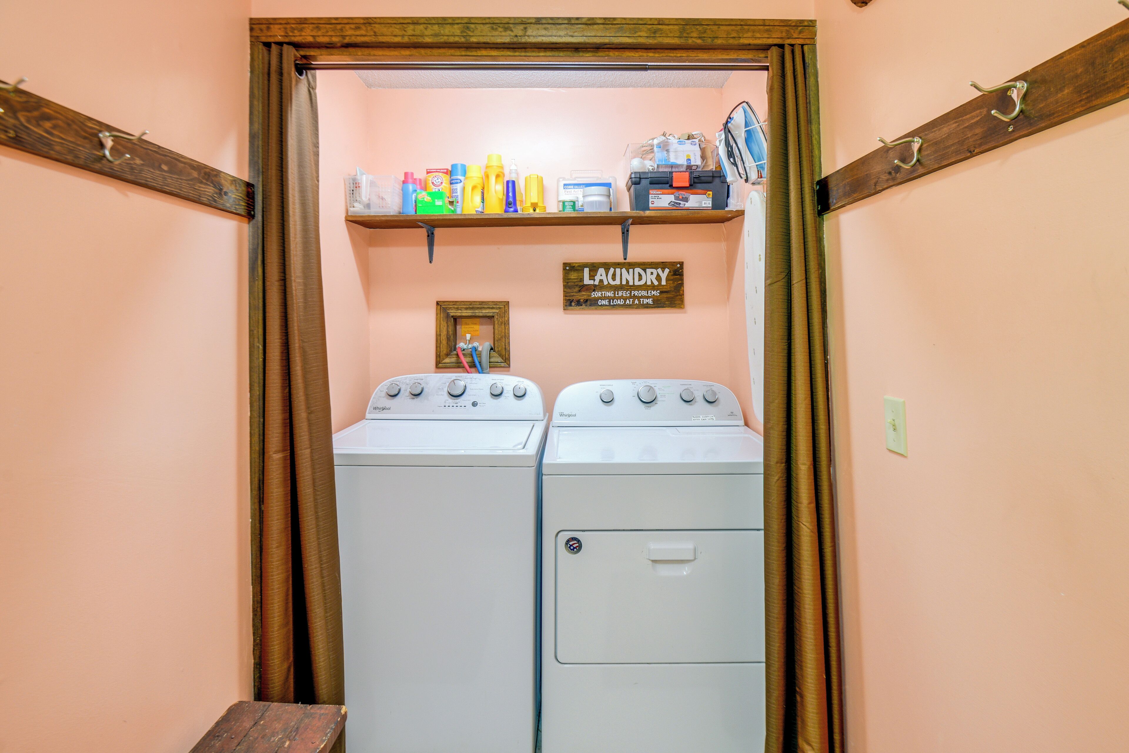 A laundry room with two washing machines, a shelf with cleaning supplies, and a sign indicating one load per time.