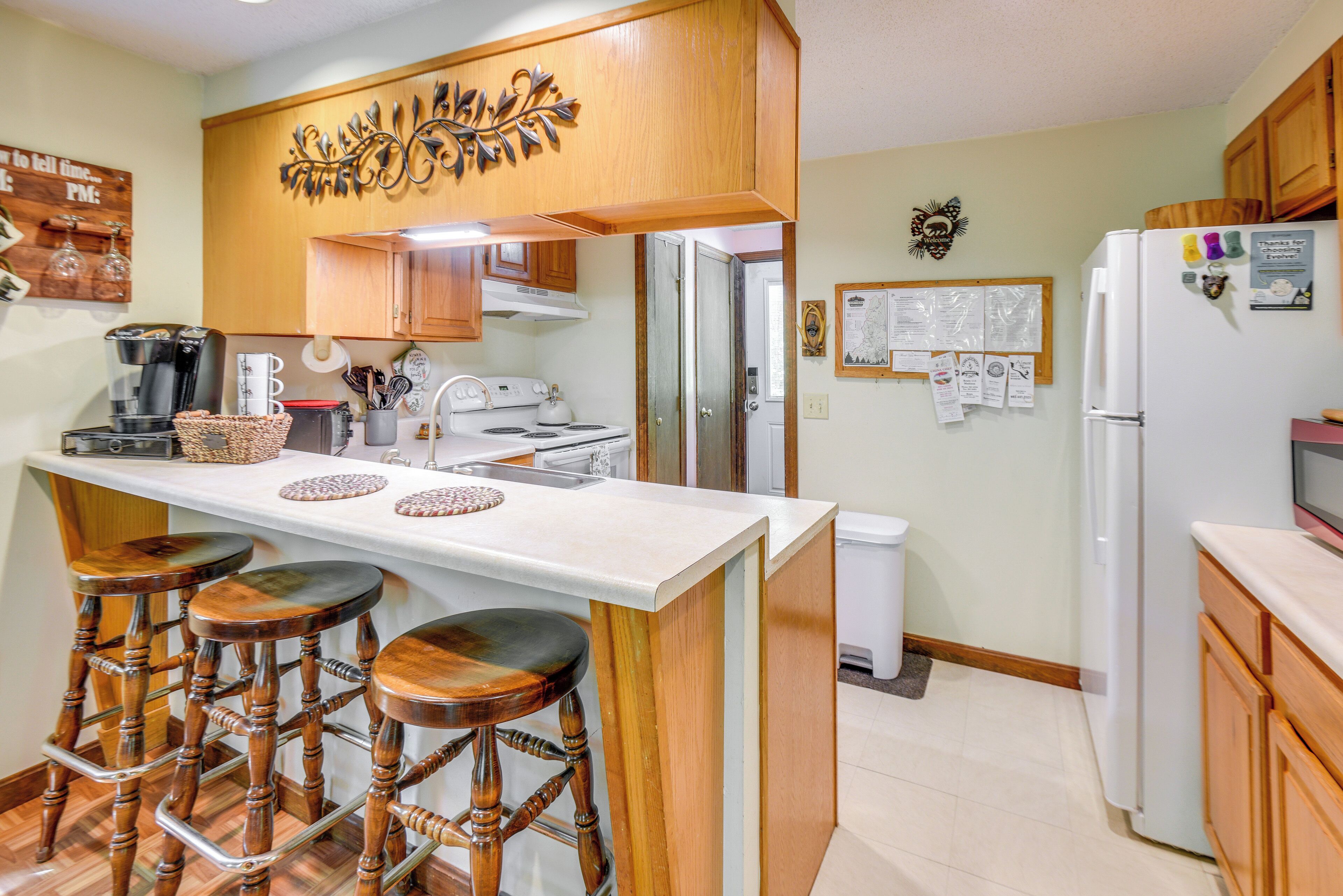 A kitchen with wooden cabinets, a white countertop, and a bar stool area.