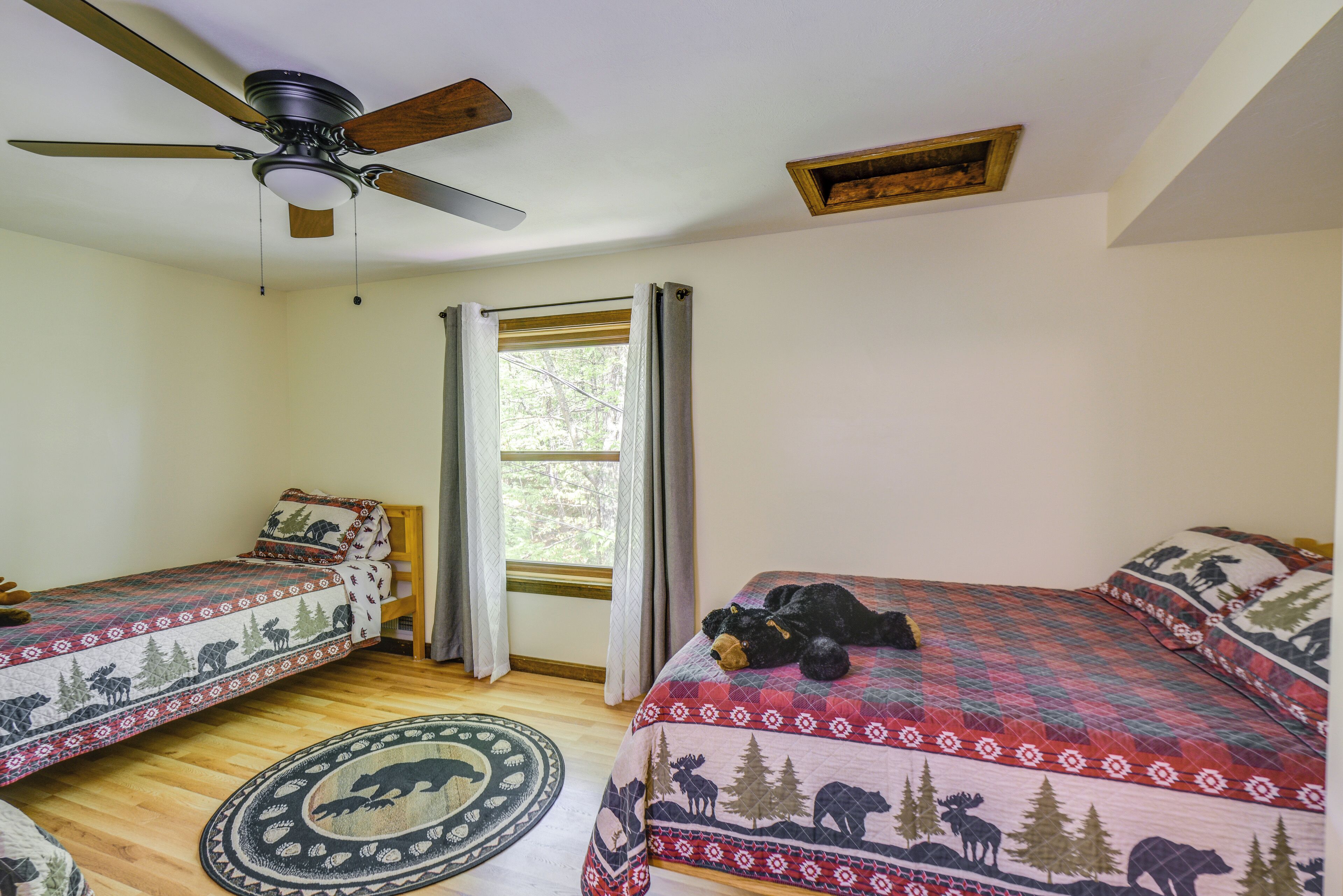 Un dormitorio con dos camas, un ventilador de techo, una ventana con cortinas y una alfombra con estampados de animales.