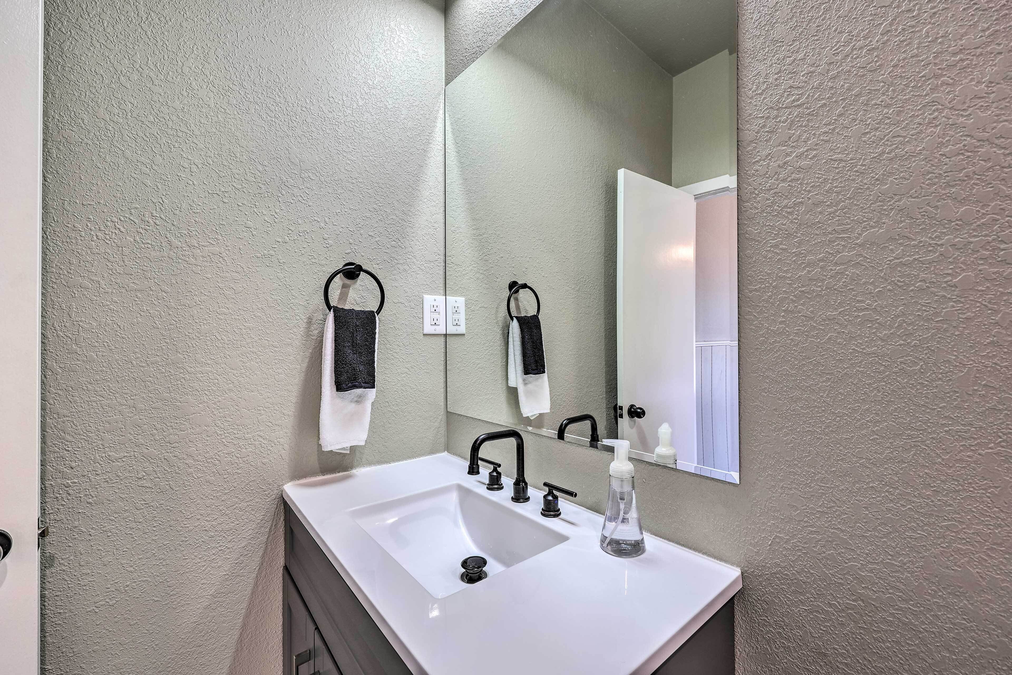 A bathroom with a white sink, black faucet, and a mirror above it. There are two towels hanging on hooks.