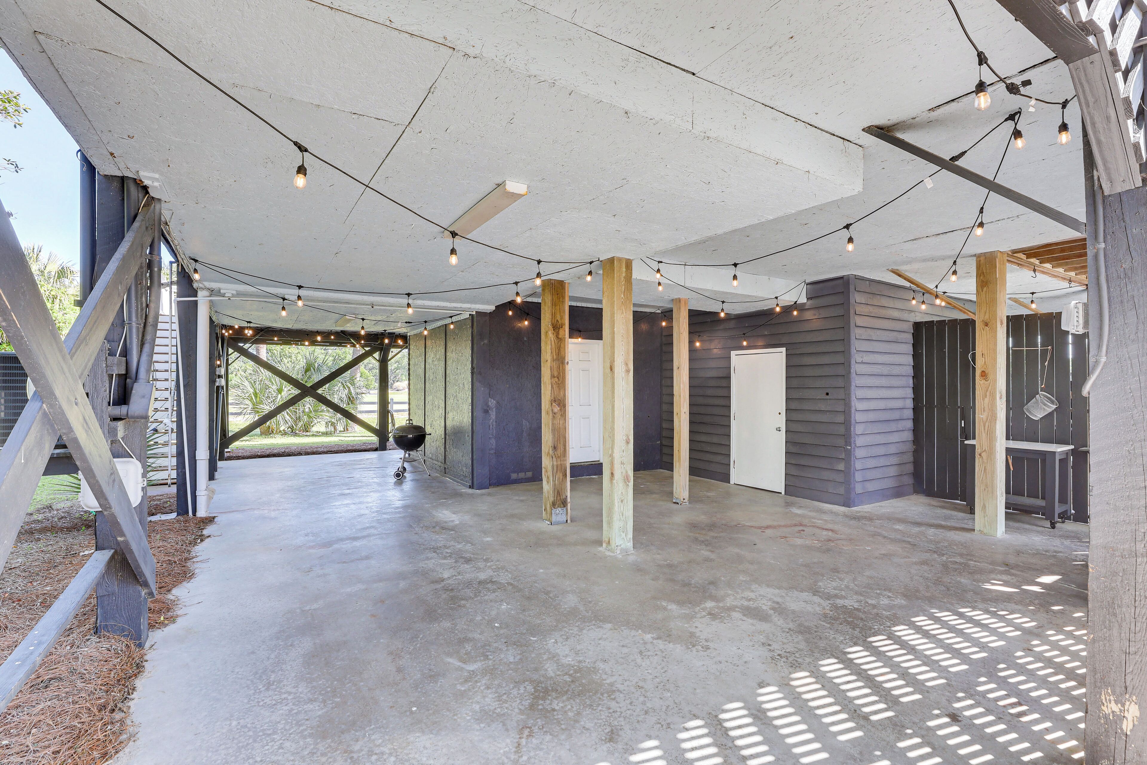 An open covered patio area with concrete flooring, wooden beams, and string lights.