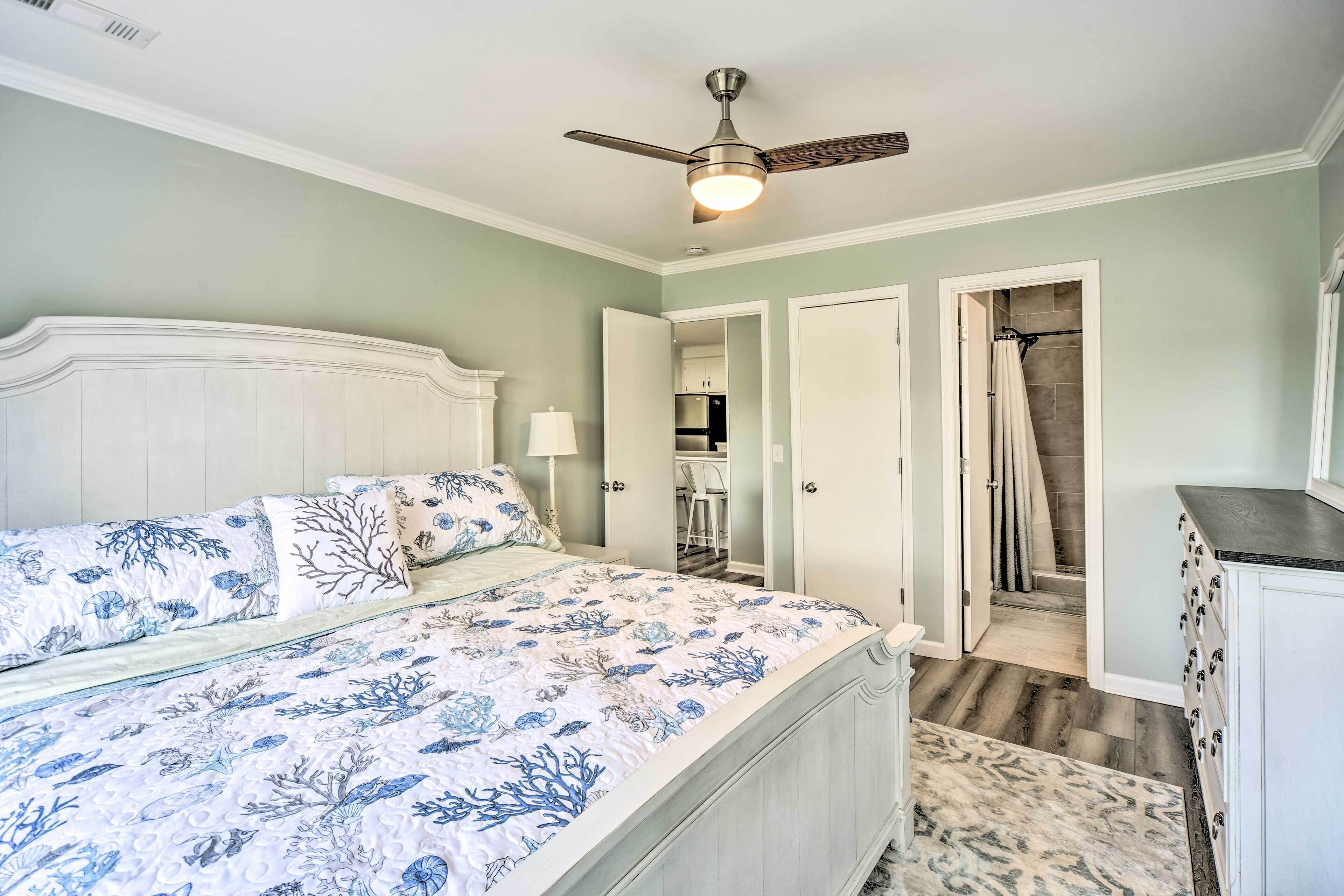 A bedroom with a bed, a ceiling fan, and a bathroom visible through an open door.