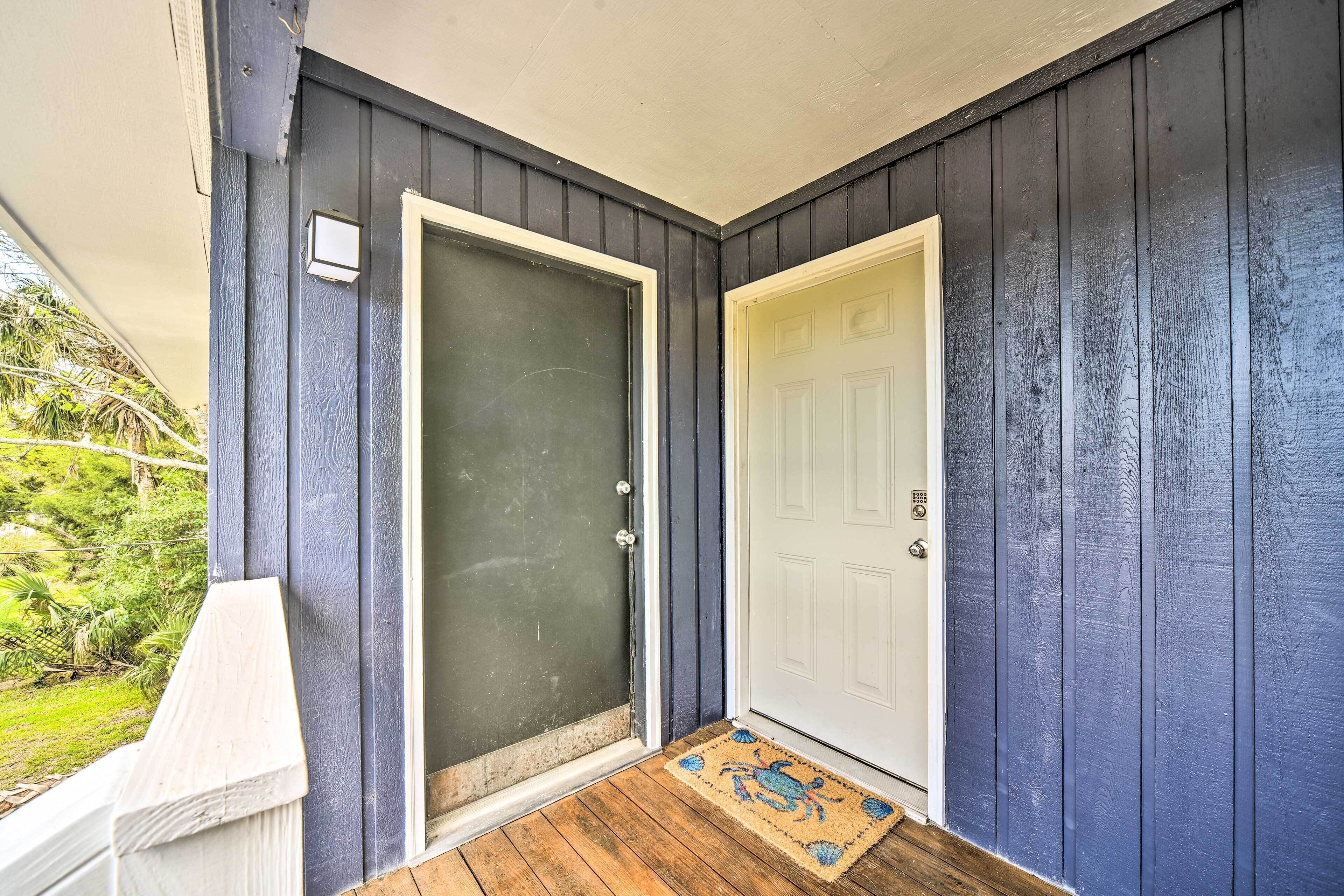 Una casa con pareti blu scuro, una porta bianca e un portico in legno con un tappetino.