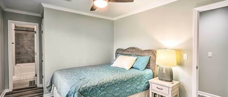 A bedroom with a bed, a nightstand, a lamp, a ceiling fan, and a door leading to a bathroom.