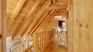 An attic room with wooden beams, a wooden railing, and a window with blinds. - Cabin w/ Catch & Release Pond in Hueytown! (Bessemer)