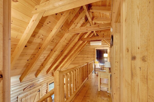 An attic room with wooden beams, a wooden railing, and a window with blinds. - Cabin w/ Catch & Release Pond in Hueytown! (Bessemer)