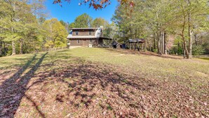 A rustic cabin with a large deck, surrounded by trees and a clear sky. - Cabin w/ Catch & Release Pond in Hueytown! (Bessemer)