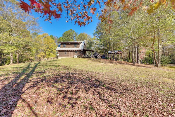 A rustic cabin with a large deck, surrounded by trees and a clear sky. - Cabin w/ Catch & Release Pond in Hueytown! (Bessemer)