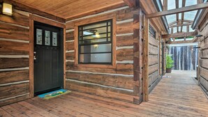 Una cabaña de troncos con fachada de madera, una puerta negra, una ventana con panel de vidrio esmerilado y piso de madera.