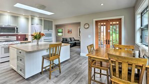 Una cocina moderna con armarios blancos, una isla central y una zona de comedor con sillas de madera.
