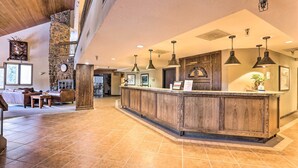 A spacious lobby with a wooden reception desk, multiple hanging pendant lights, and a stone accent wall. - Cozy Ski-in/out Winter Park Studio w/ Hot Tubs! (Winter Park)