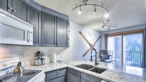 A modern kitchen with dark cabinets, a white stove, and a granite countertop. - Cozy Ski-in/out Winter Park Studio w/ Hot Tubs! (Winter Park)