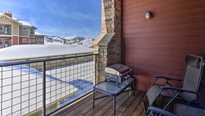 Een balkon met een barbecue, stoelen en uitzicht op een besneeuwd landschap.