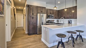 Une cuisine moderne avec des meubles en bois, des appareils en acier inoxydable, un grand îlot central doté de tabourets et un éclairage suspendu.
