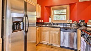 A kitchen with a stainless steel refrigerator, wooden cabinets, a dishwasher, and a window with a view of trees. - Fish, Hike & Ski: Riverfront Granby Cabin! (Granby)