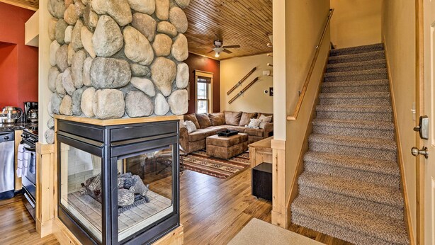 A cozy living area with a stone fireplace, a wooden ceiling, and a staircase with a carpeted landing. - Fish, Hike & Ski: Riverfront Granby Cabin! (Granby)