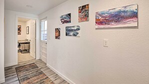 A hallway with a wooden floor, a patterned rug, and four abstract paintings on the wall.