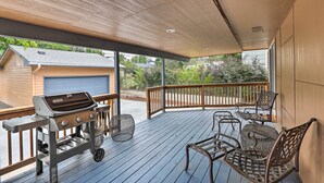 A covered outdoor deck with a grill, wicker chairs, and a view of a house in the background.