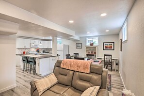 A modern living room with a leather sofa, a kitchen area with white cabinets, and a dining area with a table and chairs.
