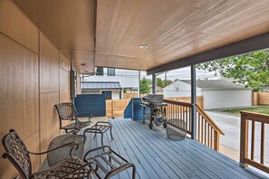 A covered outdoor deck with a grill, chairs, and a view of the neighborhood.