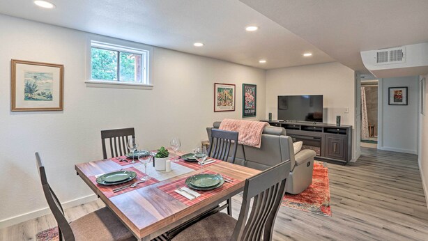 A dining area with a wooden table set for four, a gray sofa, and a TV in the background.