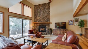 A spacious living room with leather sofas, a stone fireplace, a television, and a balcony with outdoor seating. - Deck + Mtn View: Keystone Townhome Near Resort! (Keystone)