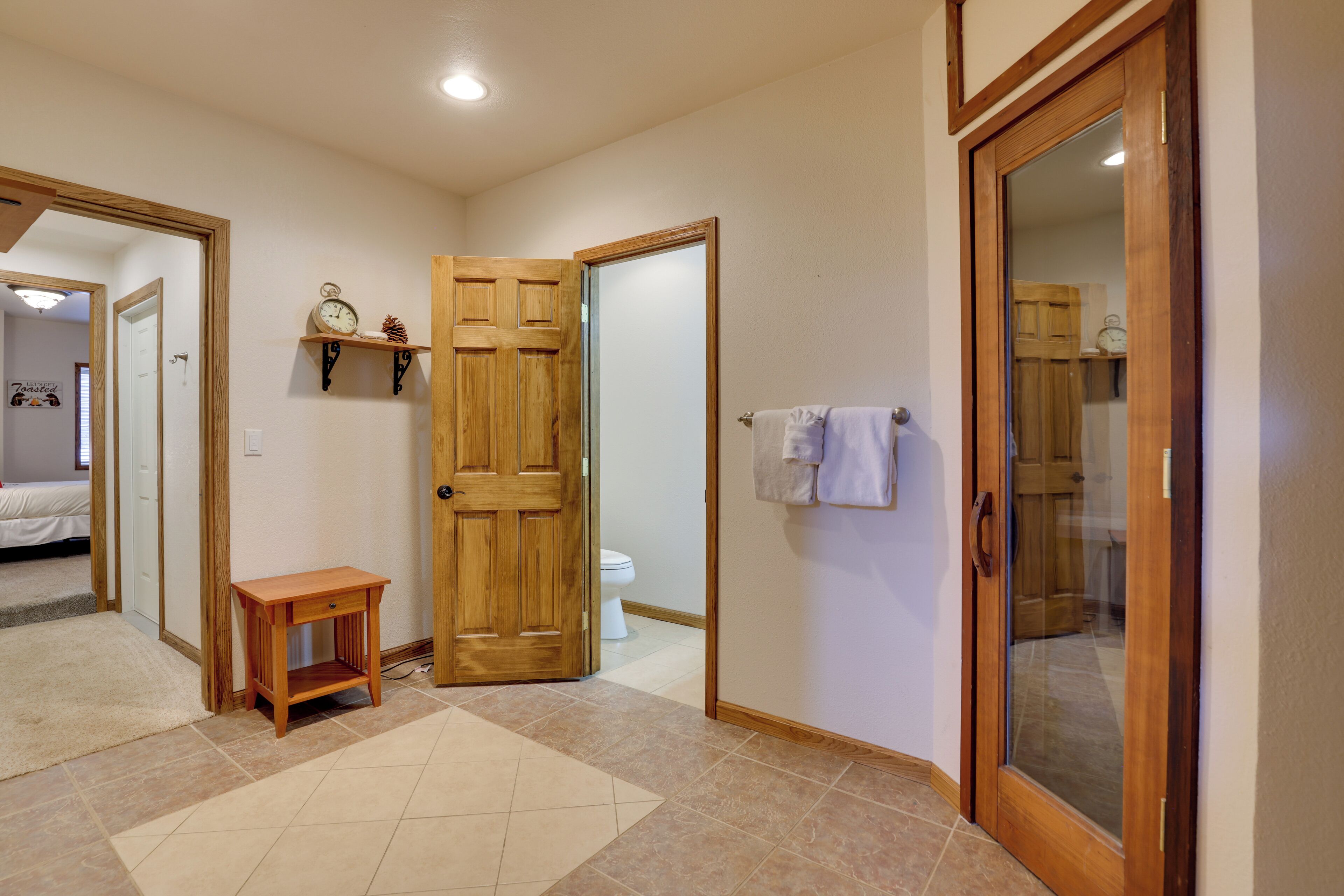 Een badkamer met een houten deur, een klein houten tafeltje, een handdoekhouder en een toilet.