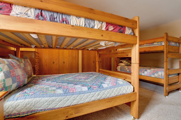 A bunk bed room with a wooden frame, a quilted bedspread, and a wooden wardrobe.