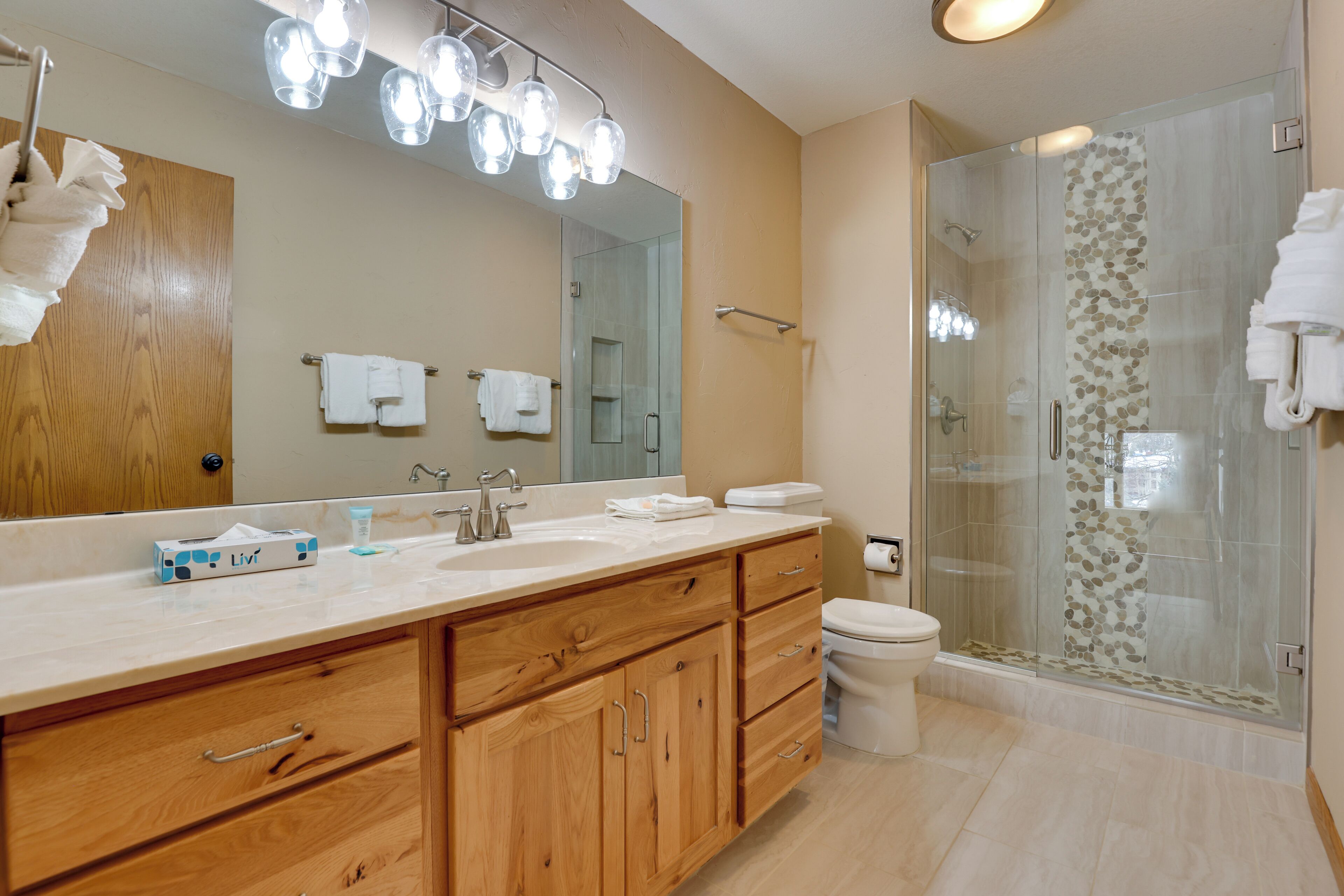 A modern bathroom with a wooden vanity, a large mirror, a glass shower enclosure, and a toilet.
