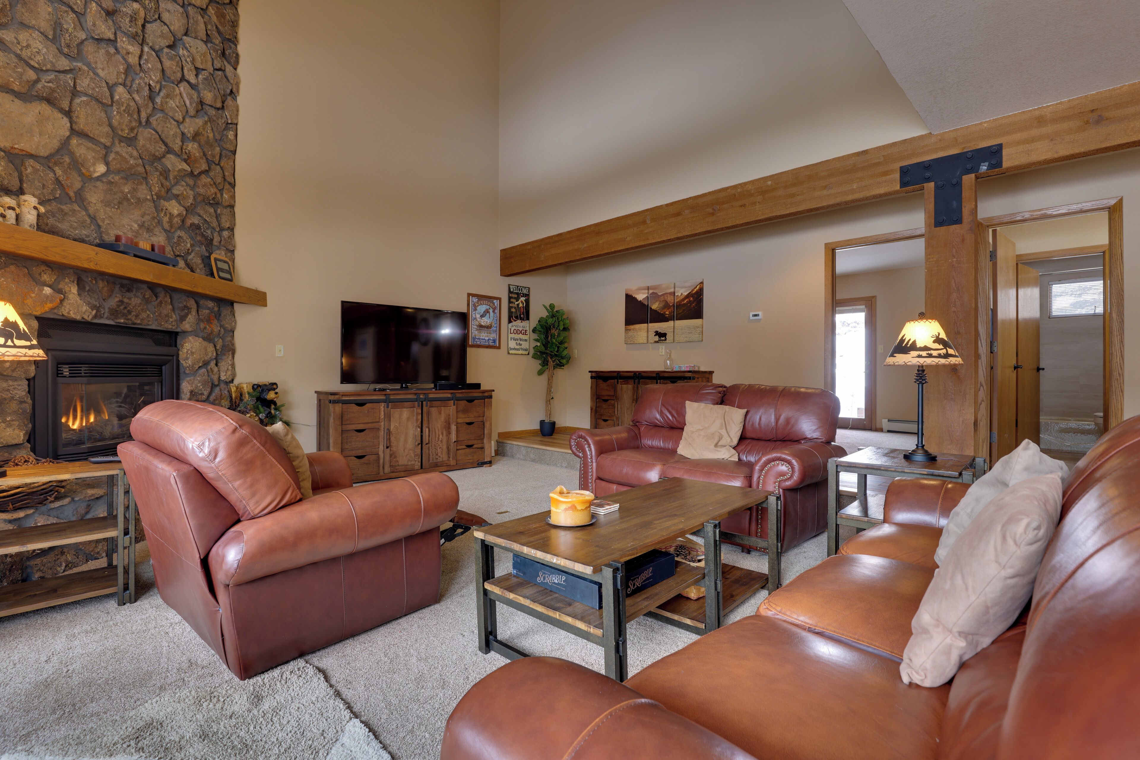 A cozy living room with leather sofas, a stone fireplace, a television, and a wooden ceiling beam.