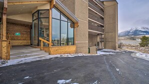Een modern gebouw met een glazen ingang, houten treden en een uitzicht op een met sneeuw bedekte berg.