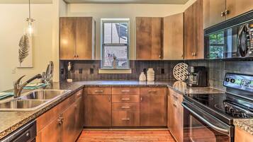 A modern kitchen with wooden cabinets, a stainless steel sink, a built-in oven, and a window with a view of the outside.