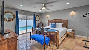 A bedroom with a large bed, a wooden chair, a desk, a TV, a ceiling fan, and a view of a swimming pool. - Home w/ Private Pool - Near Las Vegas Strip! (Las Vegas)