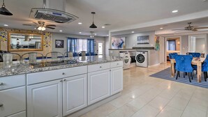 A spacious kitchen with white cabinetry, granite countertops, and a central island. There is a dining area with blue chairs and a rug. - Home w/ Private Pool - Near Las Vegas Strip! (Las Vegas)