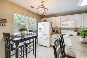 A kitchen with white cabinets, a refrigerator, a microwave, and a stove. There is a dining table with chairs and a vase with flowers. - Home Sweet Home' w/ Private Pool + Patio! (Knoxville)