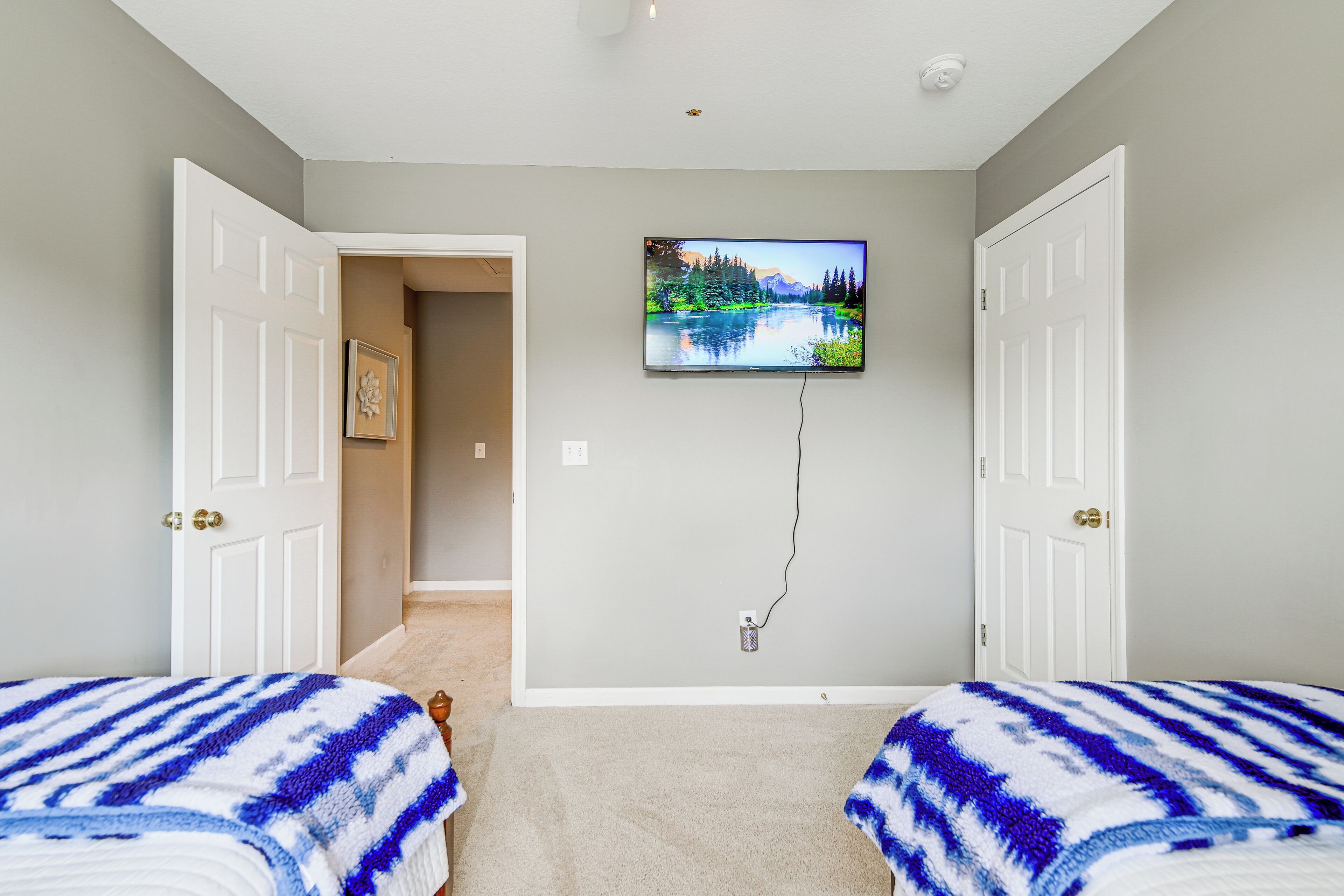 Una habitación con dos camas, un televisor montado y una puerta que da a otra habitación.