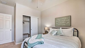 A bedroom with a bed, a nightstand, a lamp, a closet, and a motivational quote on the wall.