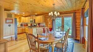 A wooden cabin interior with a dining table set for four, wooden cabinets, a chandelier, and a view through the window. - Jacksonville Cabin w/ Wraparound Deck & Views (Jacksonville)