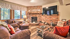 A cozy living room with a brick fireplace, leather sofas, a flat-screen TV, and a large window offering a view of trees. - 2-story Townhouse - 1 Mi to Killington Ski Area! (Killington)