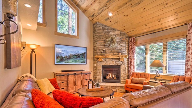 A cozy living room with a stone fireplace, leather sofa, and a television on the wall. - Luxury 4 BR Cabin: 2 King Suites on Shuttle Route (Winter Park)