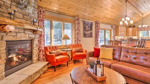 A cozy living room with a stone fireplace, leather sofa, and wooden flooring. - Luxury 4 BR Cabin: 2 King Suites on Shuttle Route (Winter Park)