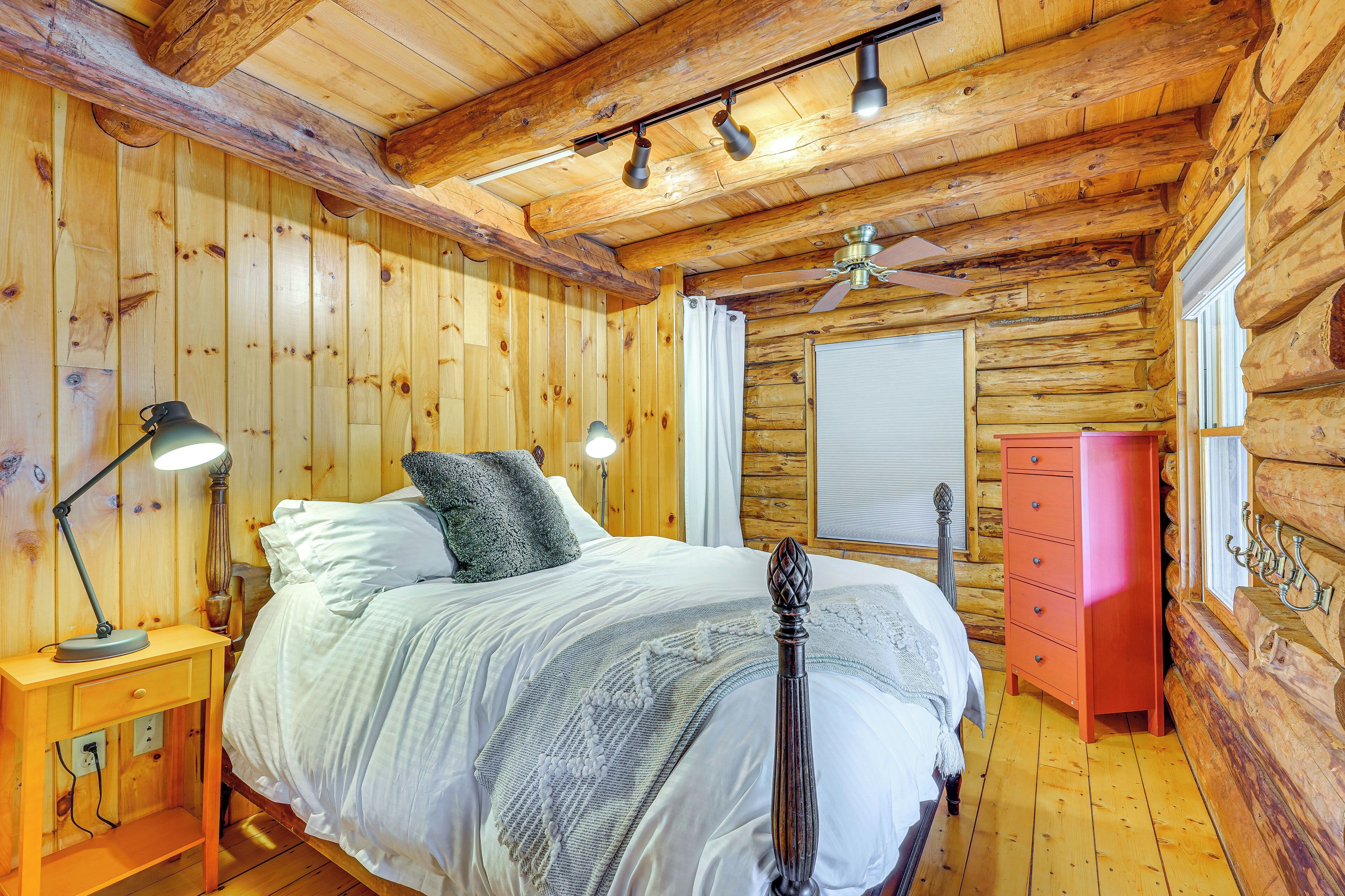 A wooden cabin bedroom with a bed, bedside lamps, a dresser, and a ceiling fan.