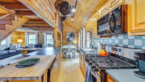 A spacious log cabin interior with a kitchen, dining area, and a cozy living room with a fireplace.