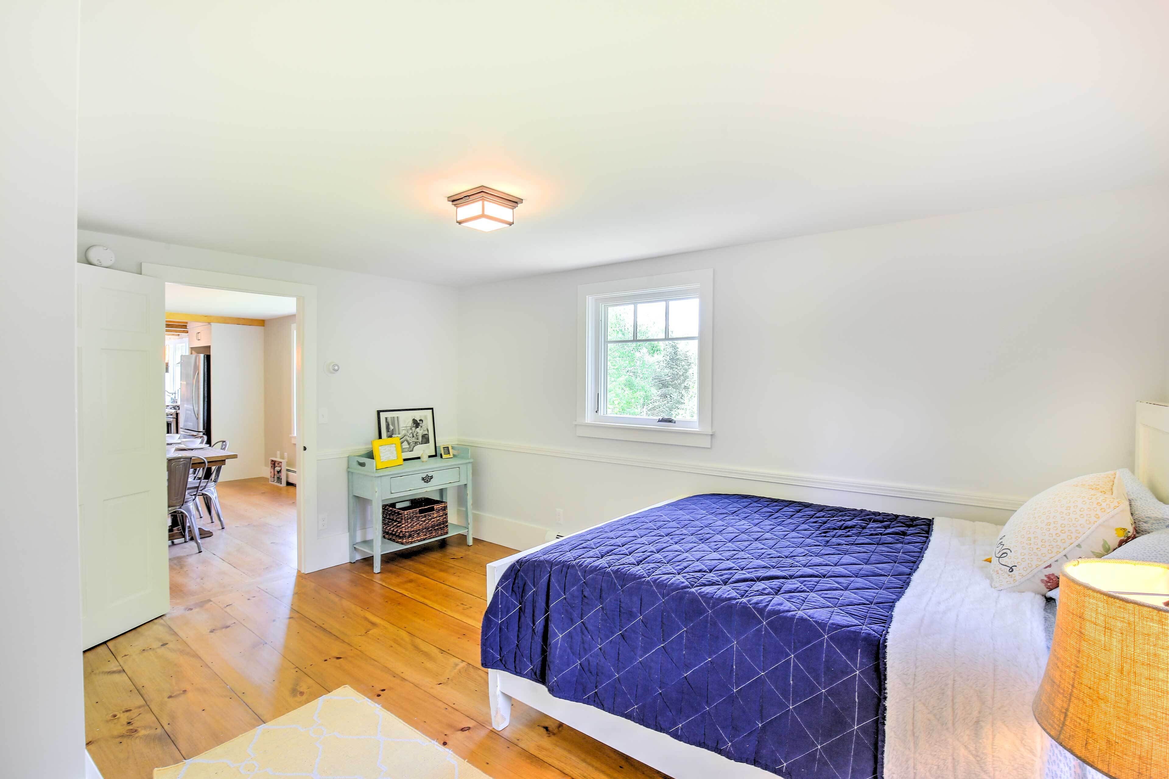 A bedroom with a bed, a window, a nightstand, and a desk area.
