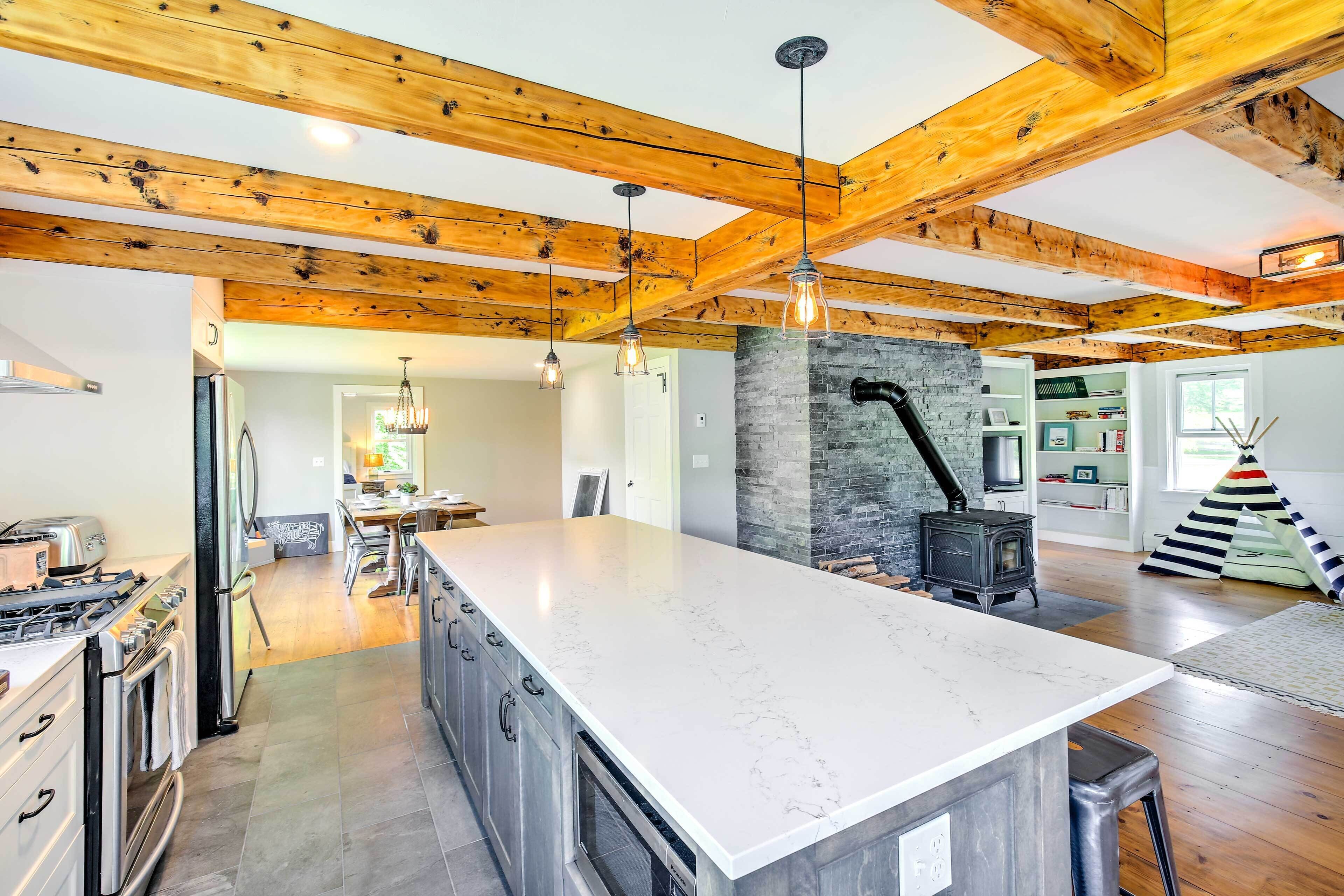 A spacious kitchen with a large island, wooden beams, and a stone fireplace.