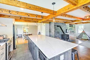 A spacious kitchen with a large island, wooden beams, and a stone fireplace. - Pet-friendly House w/ Deck - 10 Mi to Stowe Mtn! (Stowe)