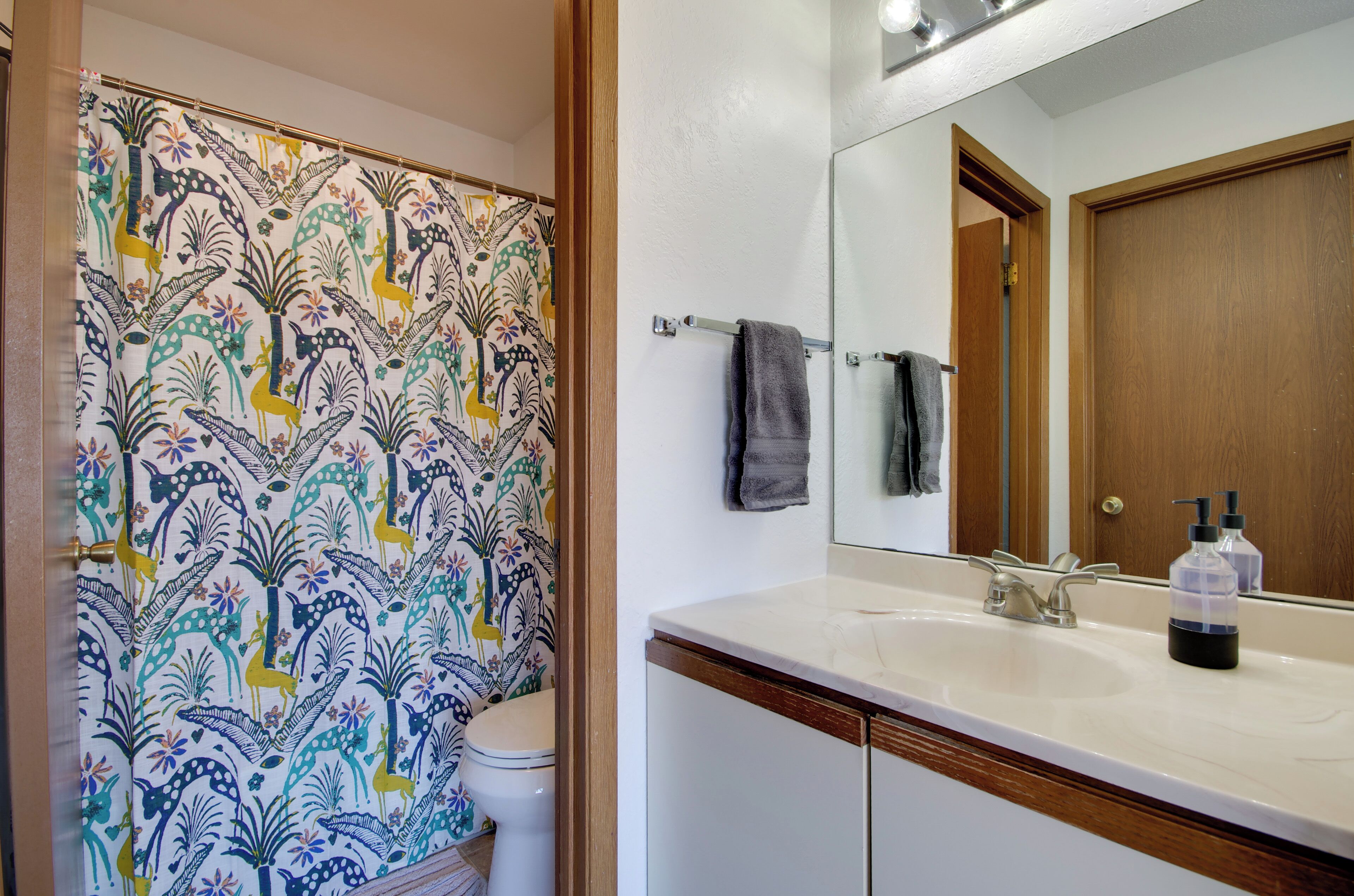 A bathroom with a patterned shower curtain, a toilet, a sink with a mirror, and a towel rack.